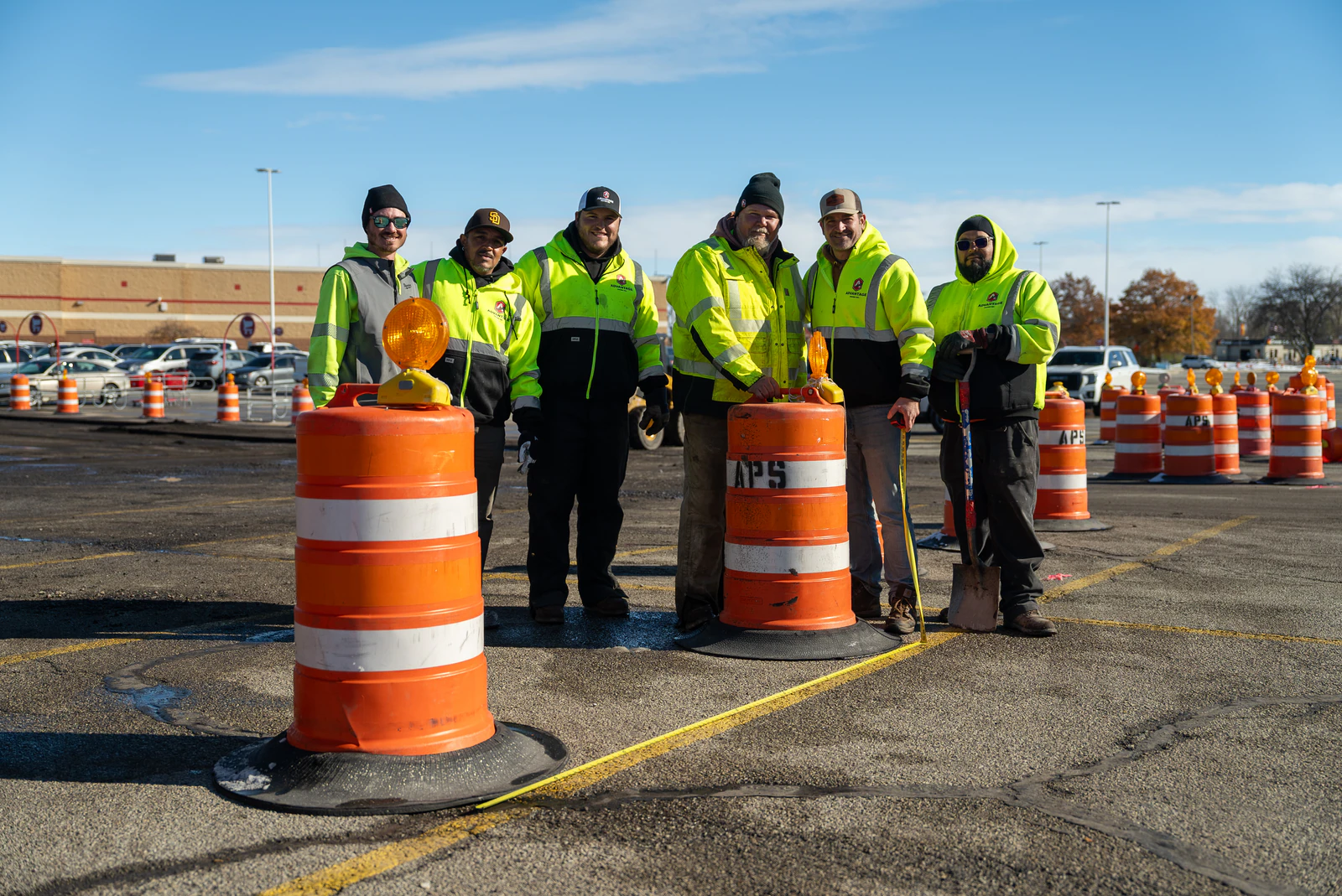 The Advantage Paving crew in high-visibility jackets standing behind traffic barrels on a freshly paved parking lot