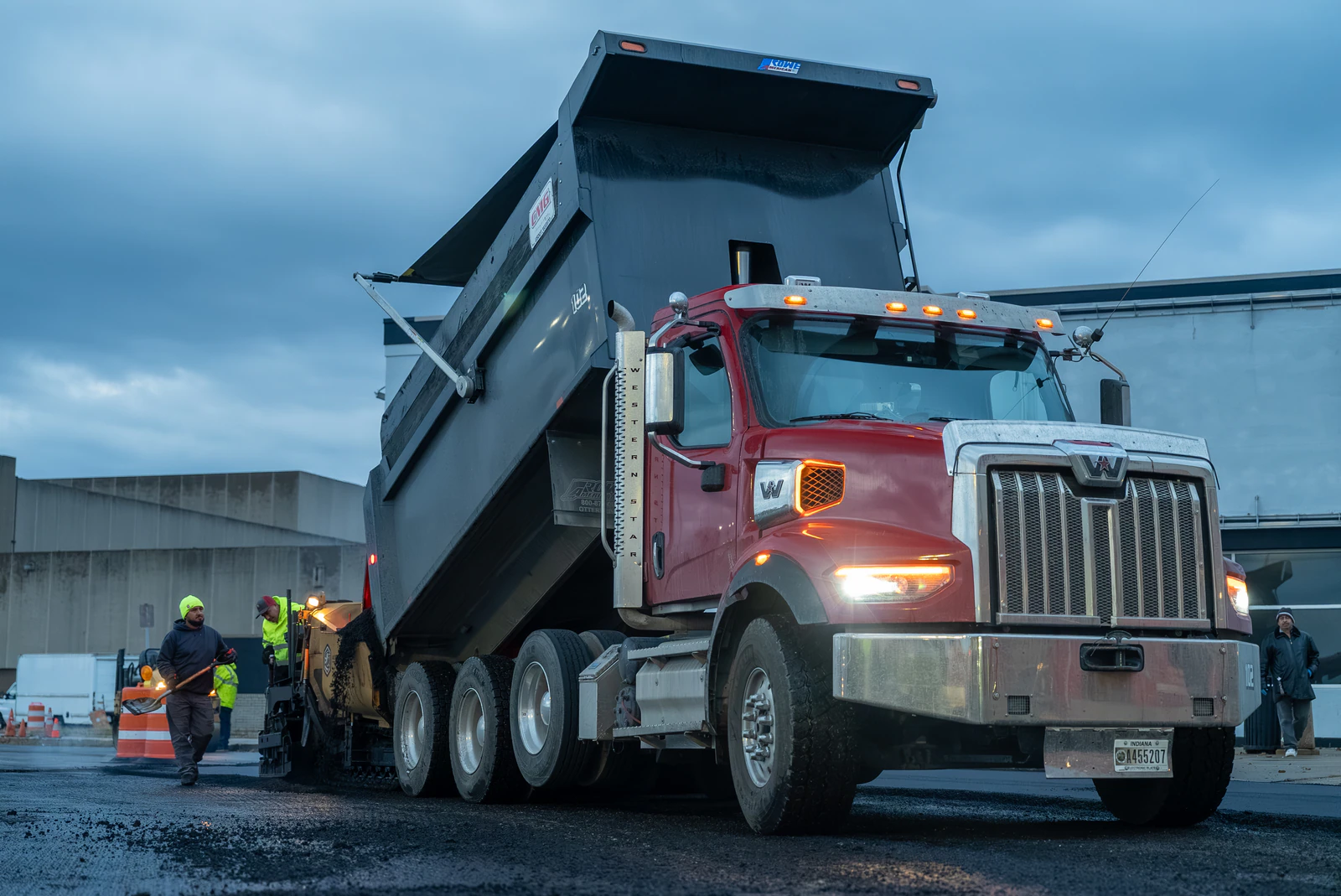 Red dump truck delivering hot-mix asphalt to the Advantage Paving crew during evening paving on a commercial lot