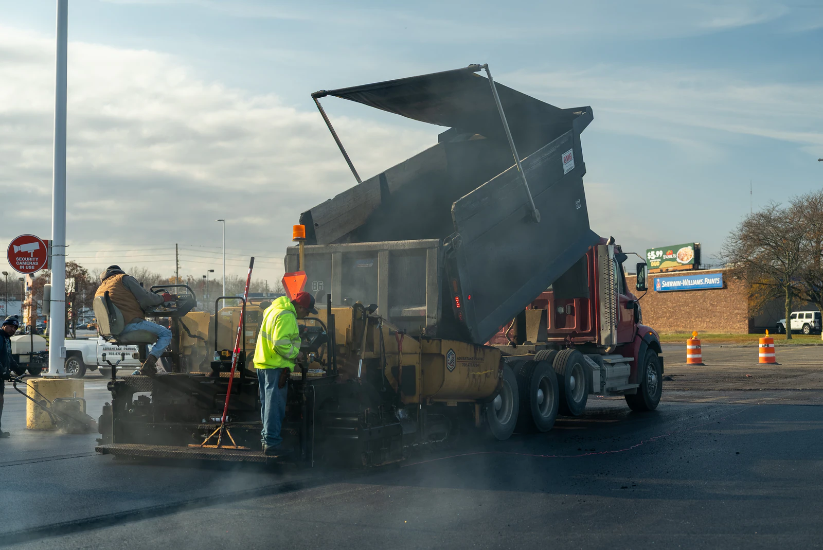 Dump truck unloading hot-mix asphalt into a paver while an Advantage Paving crew member guides the pour